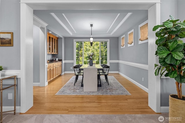 dining room featuring a tray ceiling, light wood-type flooring, and bar area