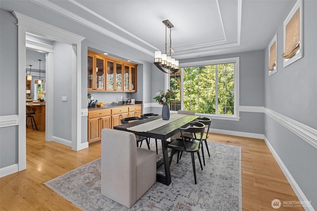 dining area featuring bar, light wood-type flooring, a raised ceiling, and baseboards