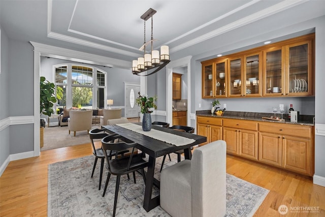 dining area featuring light wood-style floors, a tray ceiling, ornamental molding, and baseboards