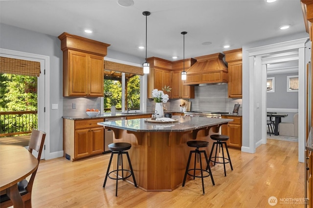 kitchen featuring custom exhaust hood, a kitchen island, light wood finished floors, brown cabinets, and recessed lighting