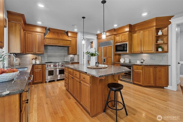 kitchen with beverage cooler, built in appliances, a sink, brown cabinets, and custom exhaust hood