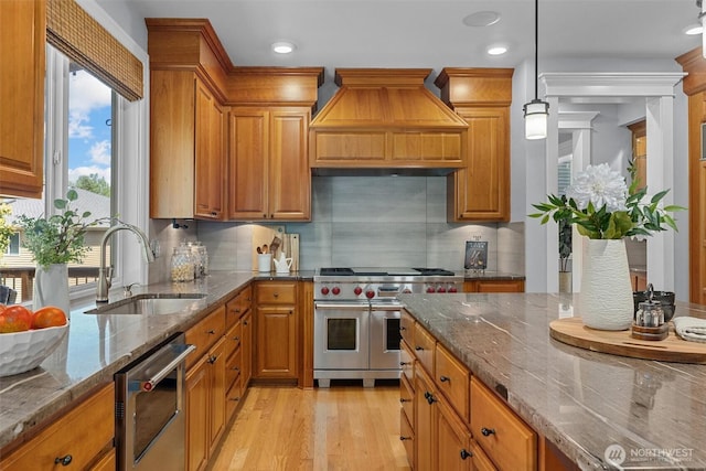 kitchen featuring double oven range, a sink, brown cabinetry, dishwasher, and light wood-style flooring