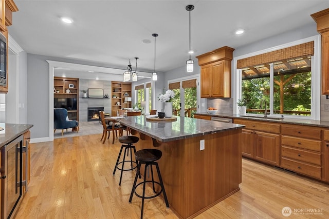 kitchen with a sink, a fireplace, a kitchen island, light wood-type flooring, and a kitchen bar