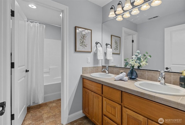 bathroom with double vanity, stone finish flooring, shower / bathtub combination with curtain, and baseboards