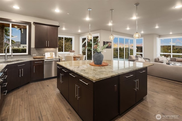 kitchen with stainless steel dishwasher, a sink, open floor plan, a kitchen island, and backsplash