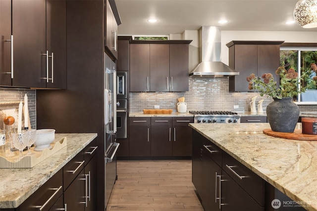 kitchen with light stone countertops, wall chimney range hood, light wood-style flooring, and dark brown cabinets