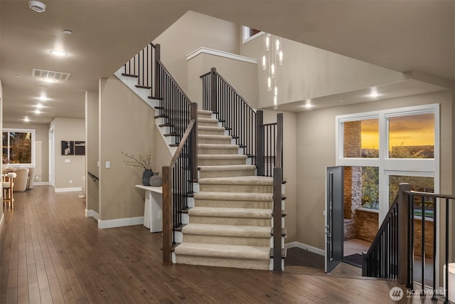 stairway featuring a high ceiling, hardwood / wood-style floors, visible vents, baseboards, and recessed lighting