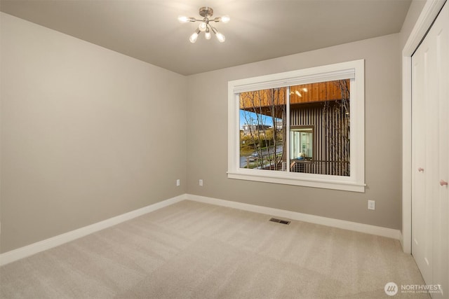 carpeted spare room featuring a chandelier, baseboards, and visible vents