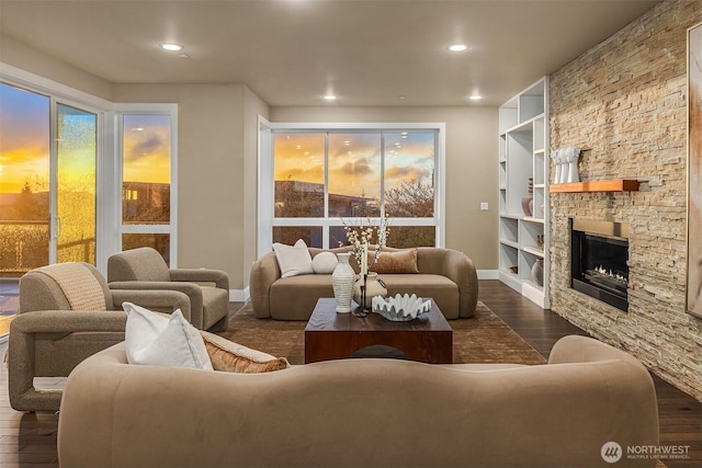 living area featuring recessed lighting, built in shelves, dark wood-style floors, baseboards, and a stone fireplace
