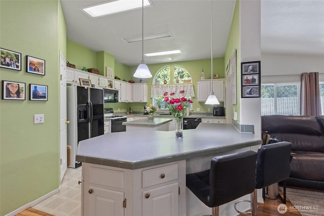 kitchen featuring pendant lighting, a breakfast bar area, open floor plan, black appliances, and white cabinets
