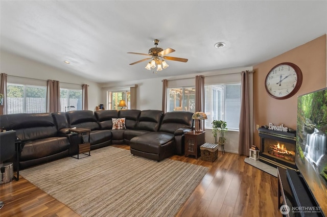living room featuring lofted ceiling, a ceiling fan, a glass covered fireplace, and wood finished floors