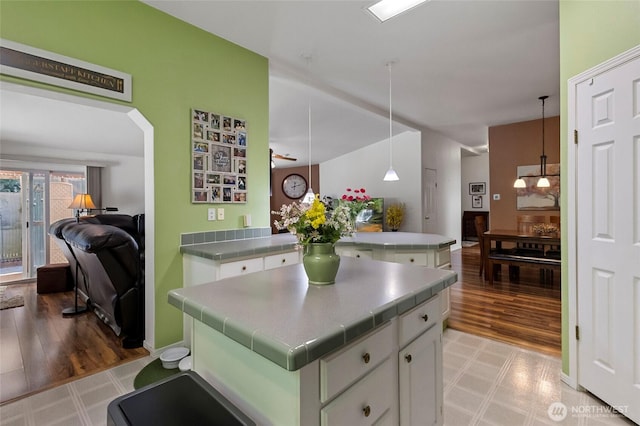 kitchen featuring light floors, decorative light fixtures, a peninsula, tile counters, and white cabinets