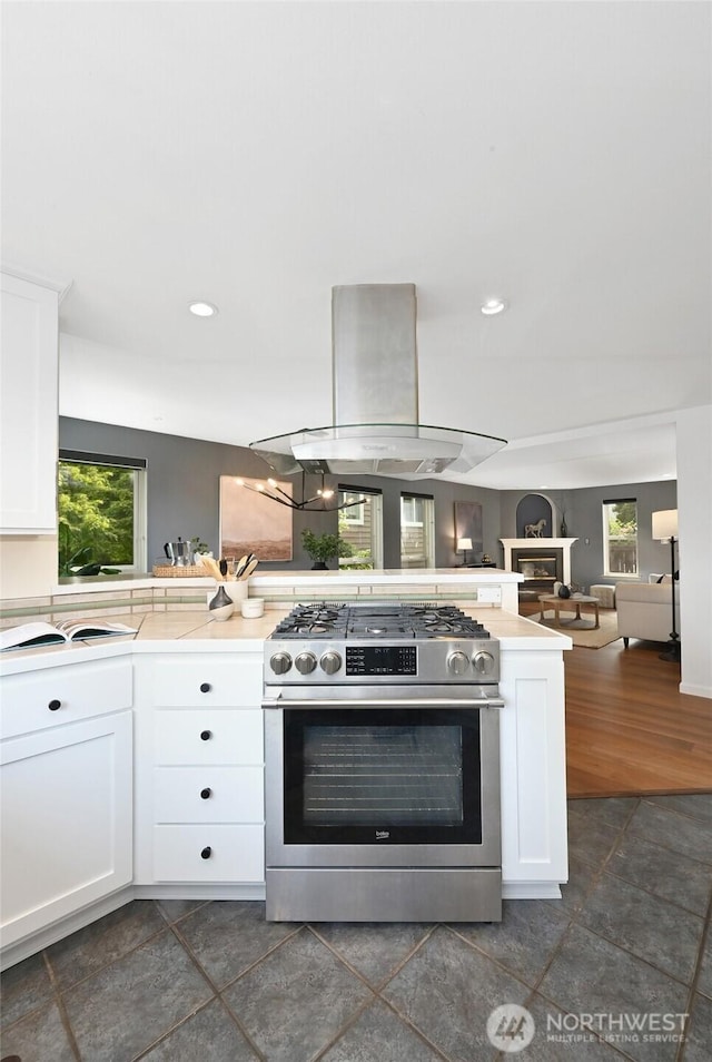 kitchen with stainless steel range with gas stovetop, island range hood, white cabinets, light countertops, and recessed lighting