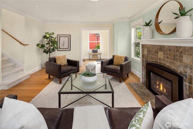 living room with wood finished floors, a fireplace with flush hearth, stairway, ornamental molding, and baseboards