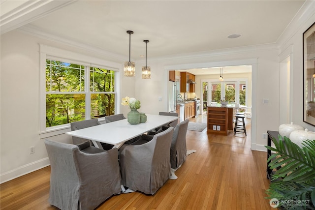dining space with healthy amount of natural light, crown molding, light wood-type flooring, and baseboards