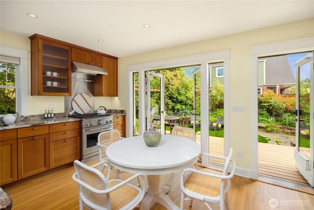 kitchen featuring stainless steel gas stove, under cabinet range hood, light wood-style flooring, glass insert cabinets, and recessed lighting