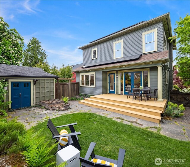 back of property featuring a deck, an outbuilding, a storage unit, roof mounted solar panels, and outdoor dining space