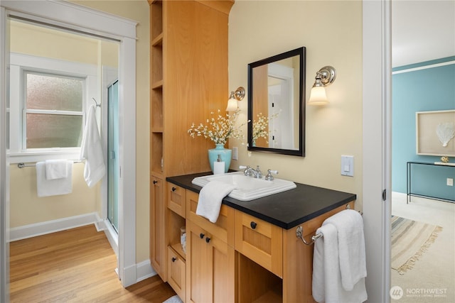 bathroom with wood finished floors, a shower stall, baseboards, and vanity