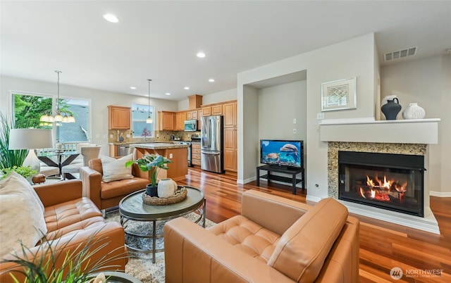 living room featuring light wood finished floors, recessed lighting, a glass covered fireplace, a chandelier, and baseboards