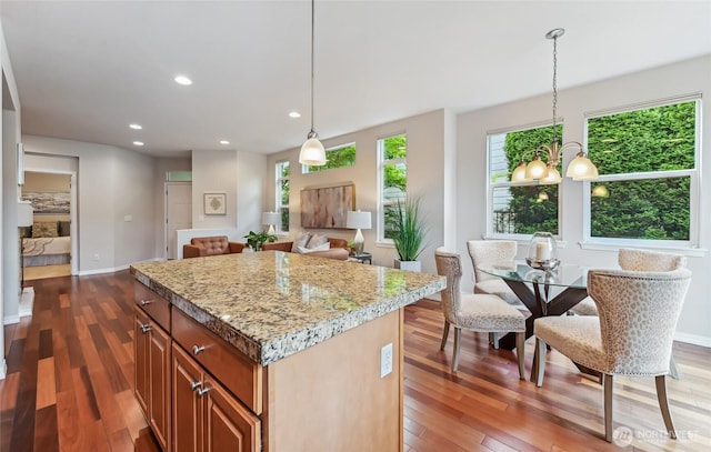 kitchen with wood finished floors, a kitchen island, open floor plan, baseboards, and recessed lighting