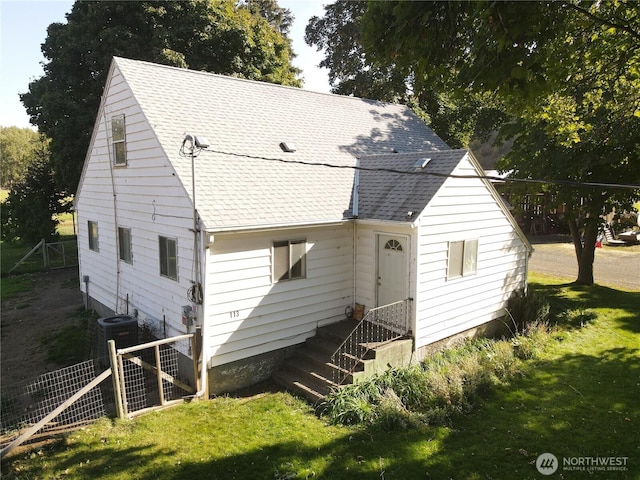 rear view of house featuring roof with shingles, fence, and a lawn