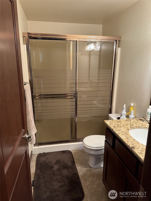 bathroom featuring a textured wall, a stall shower, toilet, and vanity
