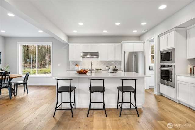 4230 336th Ave NE, Carnation, WA 98014 - kitchen with appliances with stainless steel finishes, under cabinet range hood, a kitchen bar, backsplash, and an island with sink