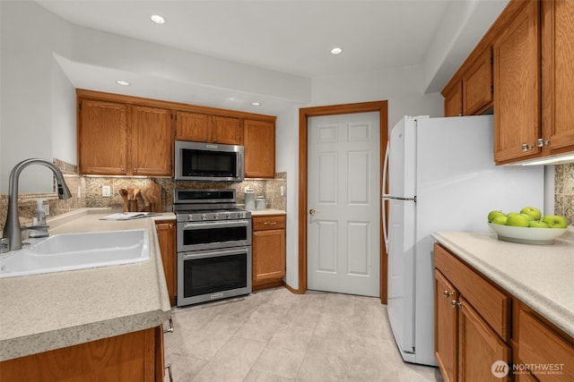 kitchen featuring appliances with stainless steel finishes, a sink, brown cabinetry, backsplash, and recessed lighting