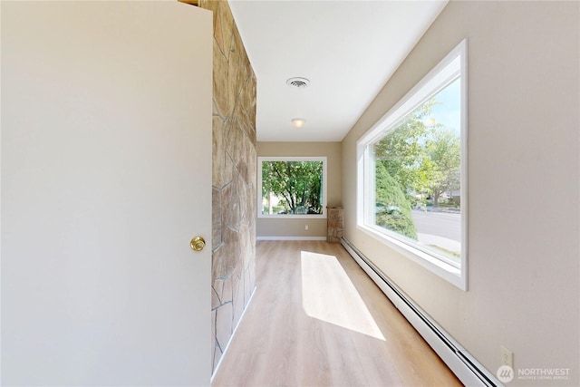 hall with light wood-type flooring, visible vents, baseboards, and a baseboard heating unit