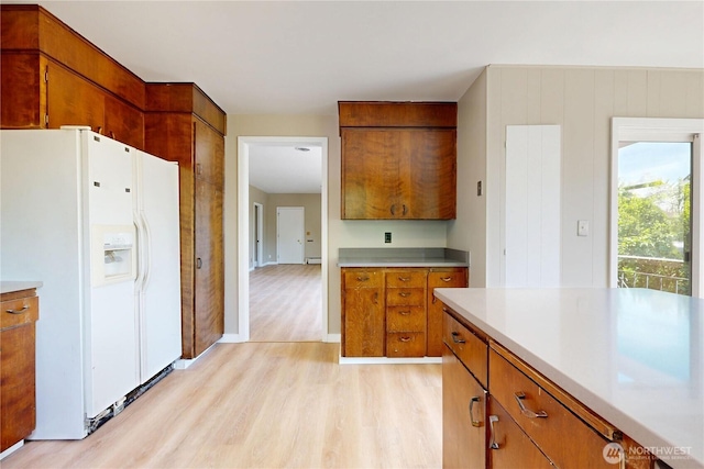 kitchen featuring light countertops, light wood-style floors, white refrigerator with ice dispenser, and brown cabinets