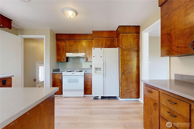 kitchen featuring white appliances, brown cabinets, under cabinet range hood, light wood finished floors, and light countertops