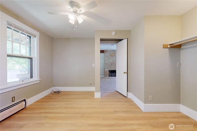interior space featuring light wood-style flooring, a ceiling fan, baseboard heating, baseboards, and a stone fireplace