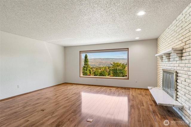 unfurnished living room with a brick fireplace, a textured ceiling, and wood finished floors