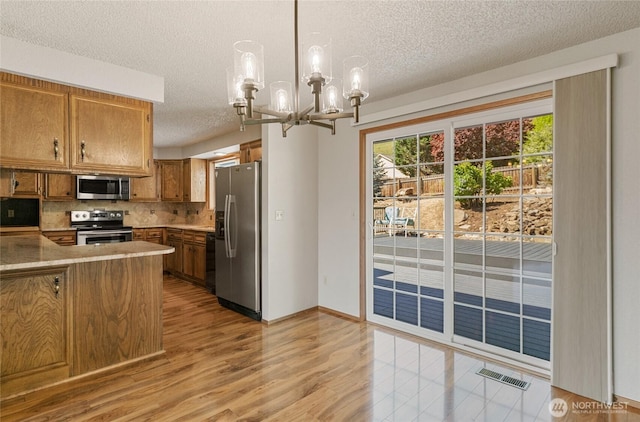kitchen with brown cabinets, stainless steel appliances, a notable chandelier, a textured ceiling, and decorative backsplash