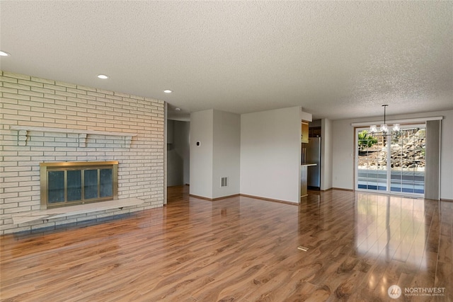 unfurnished living room with a chandelier, visible vents, a textured ceiling, and wood finished floors