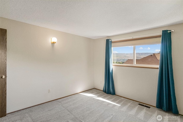 carpeted empty room featuring a textured ceiling, visible vents, and baseboards