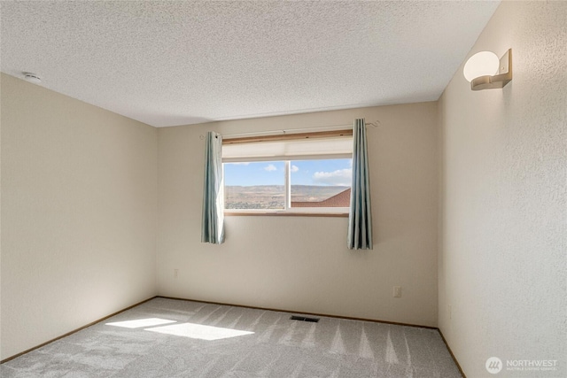 carpeted spare room featuring a textured ceiling, visible vents, and baseboards