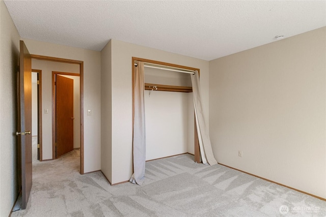unfurnished bedroom with light colored carpet, a textured ceiling, a closet, and baseboards