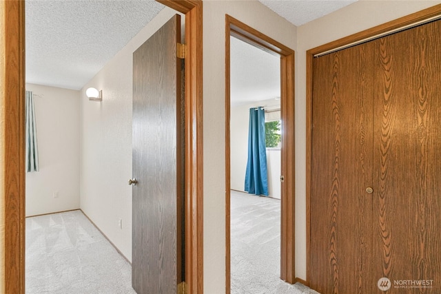corridor featuring baseboards, light carpet, and a textured ceiling