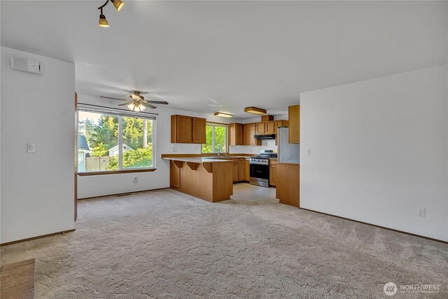 kitchen with stainless steel appliances, brown cabinets, a sink, a peninsula, and a breakfast bar