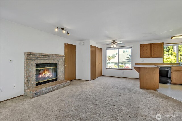 unfurnished living room featuring a sink, a fireplace, a ceiling fan, and light carpet