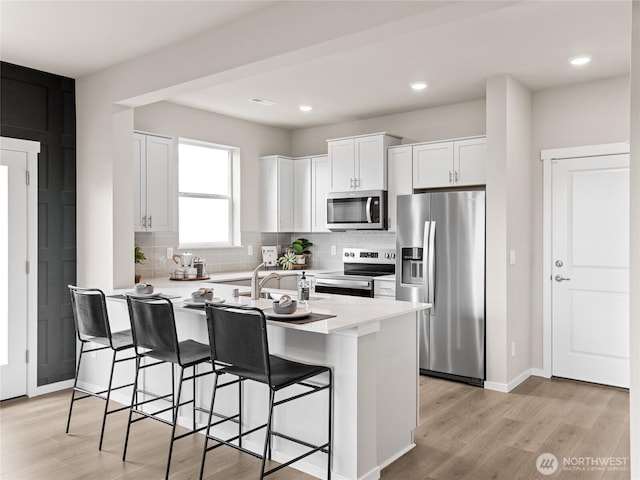 kitchen with light countertops, decorative backsplash, stainless steel appliances, and a kitchen breakfast bar