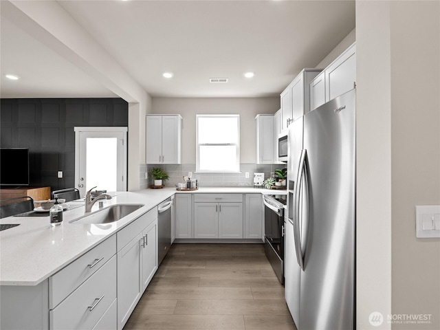 kitchen with light wood finished floors, a sink, a peninsula, white cabinets, and appliances with stainless steel finishes