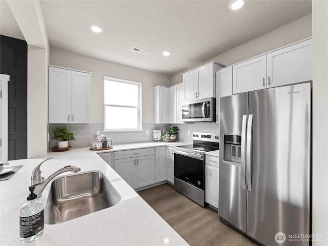 kitchen with a sink, stainless steel appliances, wood finished floors, visible vents, and decorative backsplash