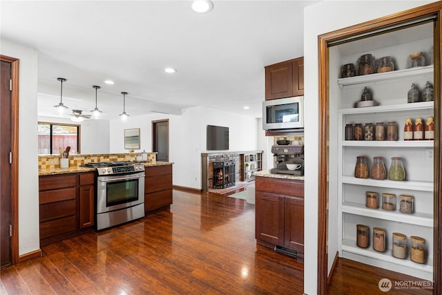 kitchen with stainless steel appliances, dark wood-style floors, a peninsula, light stone countertops, and hanging light fixtures