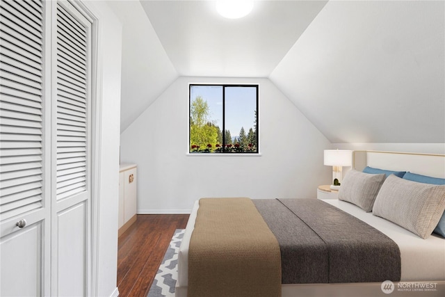 bedroom featuring dark wood-type flooring, a closet, lofted ceiling, and baseboards