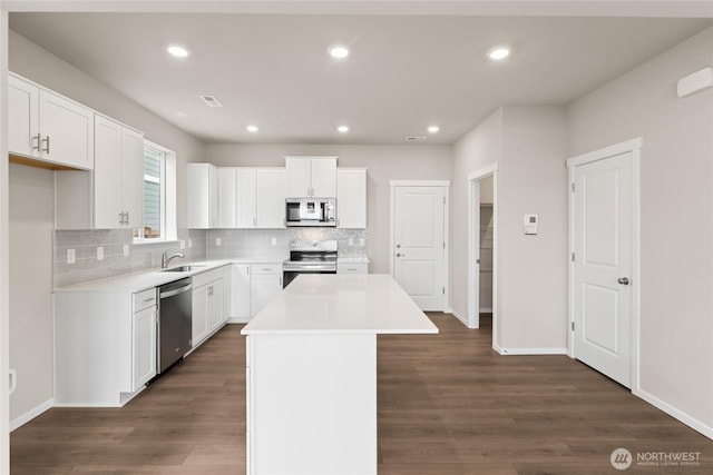 kitchen with a center island, a sink, stainless steel appliances, dark wood finished floors, and decorative backsplash
