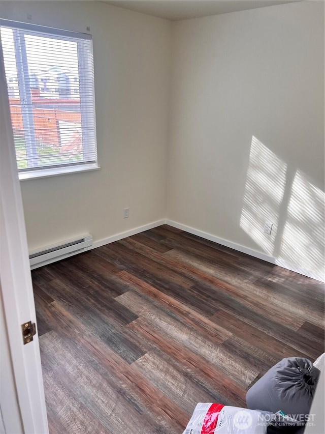 spare room featuring a baseboard heating unit, dark wood-type flooring, and baseboards