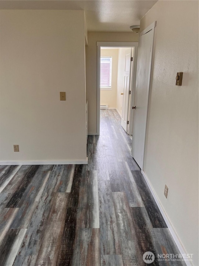 hallway featuring wood finished floors, baseboards, and a baseboard heating unit