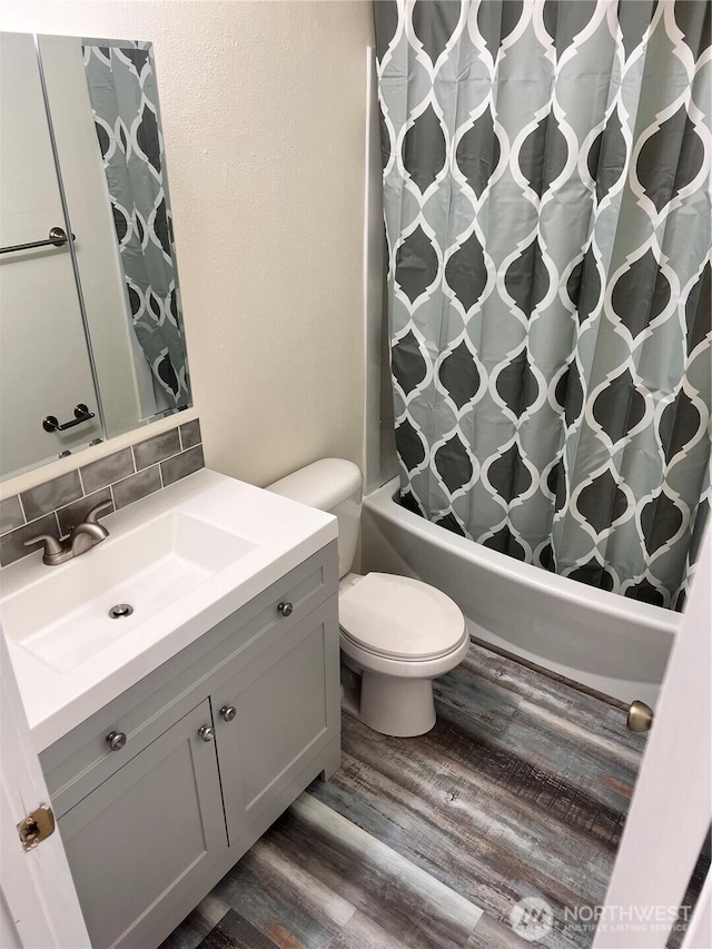 full bath with wood finished floors, shower / bath combo, vanity, toilet, and backsplash